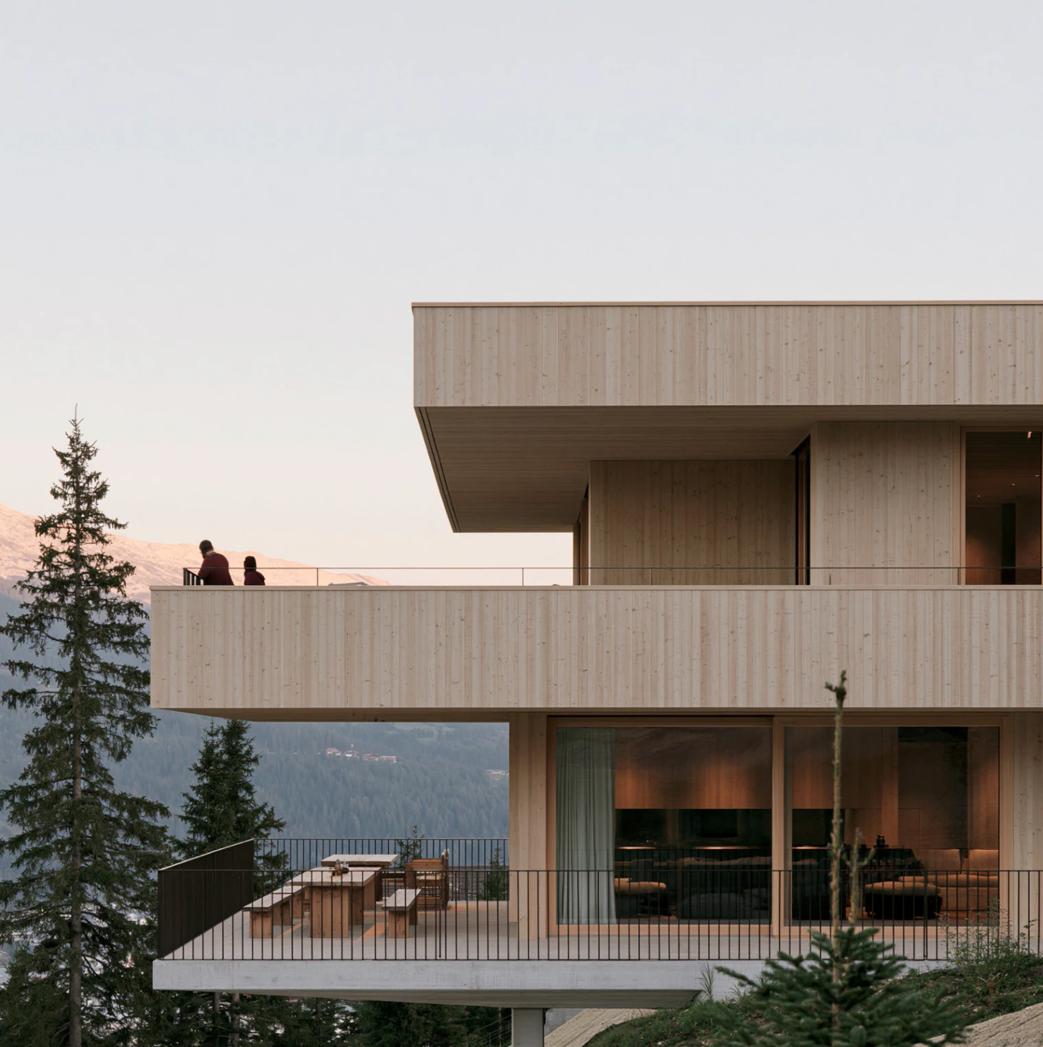 A timber and concrete house among pines, seen from below at dusk.